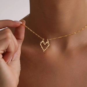 Detail of a gold heart-shaped flame pendant necklace worn on a model's neck