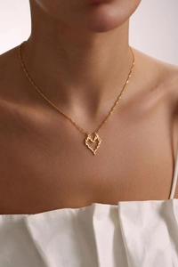 Golden heart pendant necklace with flame texture shown on model's neck for elegant look
