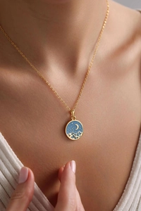 Macro detail of gold necklace with round blue enamel starry sky and mountain pendant
