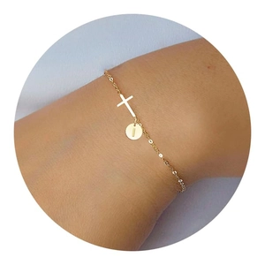 Detailed view of a gold cross bracelet with an initial I round charm on a woman's wrist