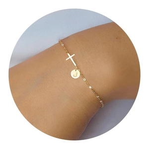 Close-up of golden cross bracelet with round letter J charm on female wrist
