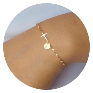 Close-up of golden cross bracelet with a round pendant engraved with the letter L