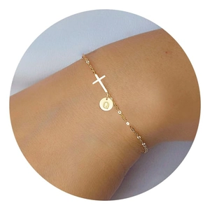 Detail of gold cross bracelet with round letter Q charm on woman's wrist