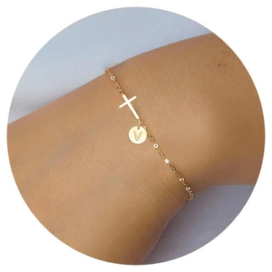 Detailed close-up of gold chain bracelet with cross charm and engraved letter V disk