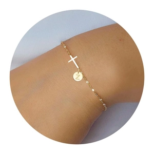 Detail of gold cross bracelet with personalized Z letter round charm on wrist