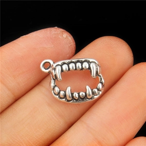 Gothic vampire fangs pendant in vintage silver alloy shown held by hand on black background