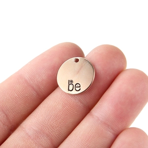 Macro detail of rose gold round charm with engraved 'be' text for DIY jewelry making