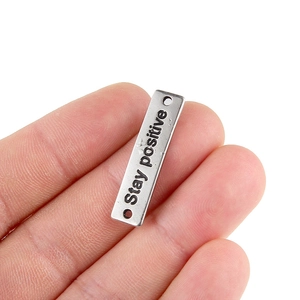 Close-up of antique silver rectangular charm with Stay positive engraving and dual side holes
