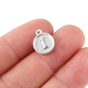 Vista macro di un ciondolo circolare argento con lettera I a rilievo e gancio