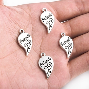 Quatre pendentifs cœur en argent antique avec gravure Friends présentés en main