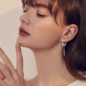 Close-up of a silver feather drop earring worn by a model showcasing detailed leaf texture
