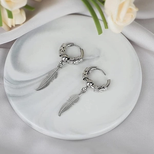 Detail shot of silver feather drop earrings with engraved hoops on marble and silk