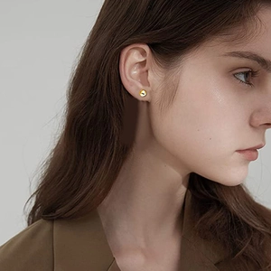 Détail d'une boucle d'oreille dorée avec motif de vis portée sur une oreille féminine