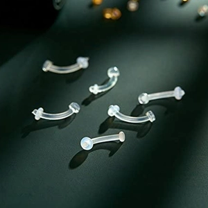 Set of clear bio-flex curved eyebrow rings and lip retainers on a dark textured background