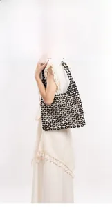 Detail view of black and white geometric beaded shoulder bag on a beige dress