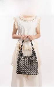 Detailed view of black beaded tote bag with beige lining worn over a white dress