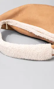 Close-up of brown pebbled leather shoulder bag featuring plush white faux fur trim and gold zipper