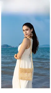 Detail of handmade beige wood bead bag with shoulder strap against a sunny beach background