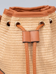 Sac seau en paille avec garniture en cuir marron et anneaux dorés sur fond gris neutre