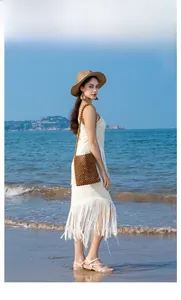 Model trägt eine braune handgefertigte Perlenumhängetasche am sonnigen Strand