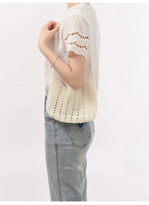 Détail d'un sac à bandoulière fait main en perles blanches porté par un mannequin élégant