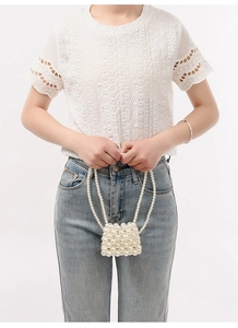 Close-up of handmade white pearl woven crossbody bag held by a fashion model