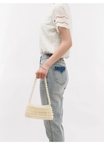 Close-up of handmade cream pearl beaded handbag held by a model for a beach vacation look
