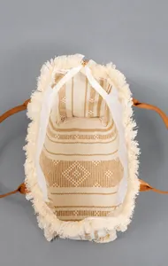 Macro view of beige canvas tote featuring fringe details and spacious inner compartment