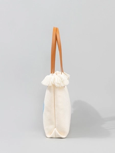 Bolso tote tejido bohemio con flecos y asas de cuero marrón sobre un fondo gris claro