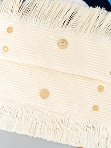 Primer plano detallado de un bolso tote bohemio en tejido crema con flecos y botones