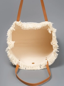 Large beige woven canvas tote bag with tassel trim and brown leather handles for beach vacation
