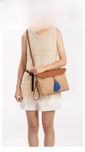 Detail of khaki straw crossbody bag featuring brown leather flap and blue tassel accent