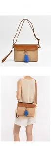 Detail of straw woven crossbody bag with brown leather trim and blue tassel pendant