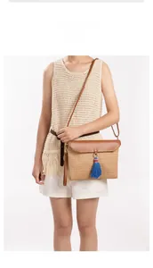 Straw woven crossbody bag featuring deep brown leather flap and blue tassel detail