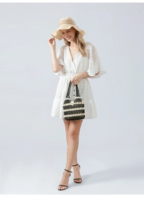 Detail of a white lace V-neck dress with ruffle sleeves and a beaded woven handbag