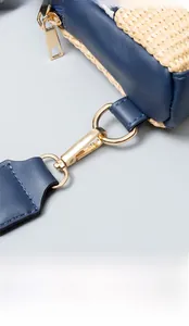 Detail view of woven straw bag with navy blue leather trim and golden metal hardware