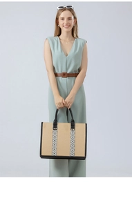 Detail view of woven straw tote bag featuring black leather handles and geometric ribbon