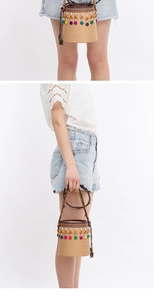 Detail of straw woven bucket bag featuring colorful tassels and wooden bead handles