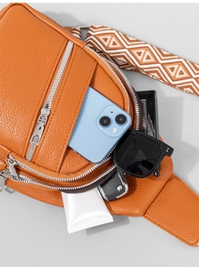 Detail view of orange textured leather crossbody bag with ethnic pattern strap and multi-zippers