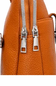 Detalle de bolso bandolera de piel PU naranja con cremalleras metálicas plateadas