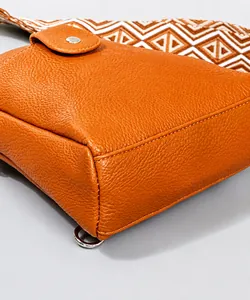 Detalle de bolso bandolera naranja de cuero granulado con correa tejida geométrica y plata