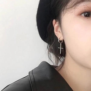 Gros plan d'une boucle d'oreille croix en acier inoxydable portée avec un look punk