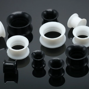Écarteurs d'oreilles en silicone noir et blanc de tailles variées sur fond réfléchissant
