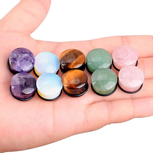 Polished natural stone ear plugs set with black O-rings held in hand for size reference