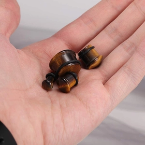 Detailed view of round tiger eye stone ear gauges with black O-rings on a hand