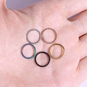 Detail of five twisted stainless steel piercing rings in varied colors held on a palm