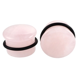 Macro detail of rose quartz stone ear plugs with black rubber O-rings on white surface