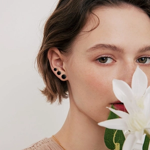 Close-up of three black minimalist round stud earrings worn by a model in a set