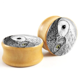 Double flared wood ear plugs with artistic owl design on a clean white background
