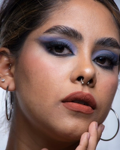 Primer plano de un aro de septo plateado y pendiente de aro en modelo con maquillaje azul